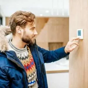 Man adjusting temperature with thermostat at home