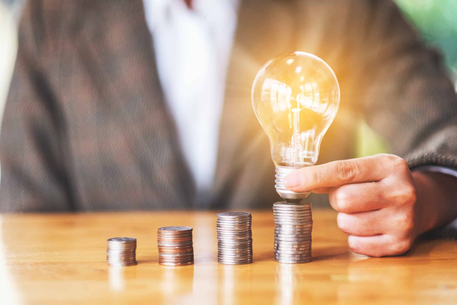 Businesswoman holding and putting lightbulb on coins stack on table